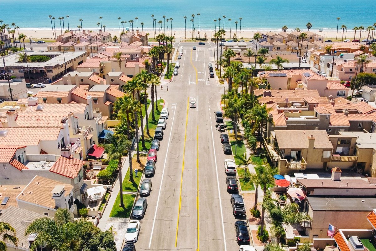 Aerial view of a sunny Orange County coastal street lined with Mediterranean homes and palms leading to the beach.