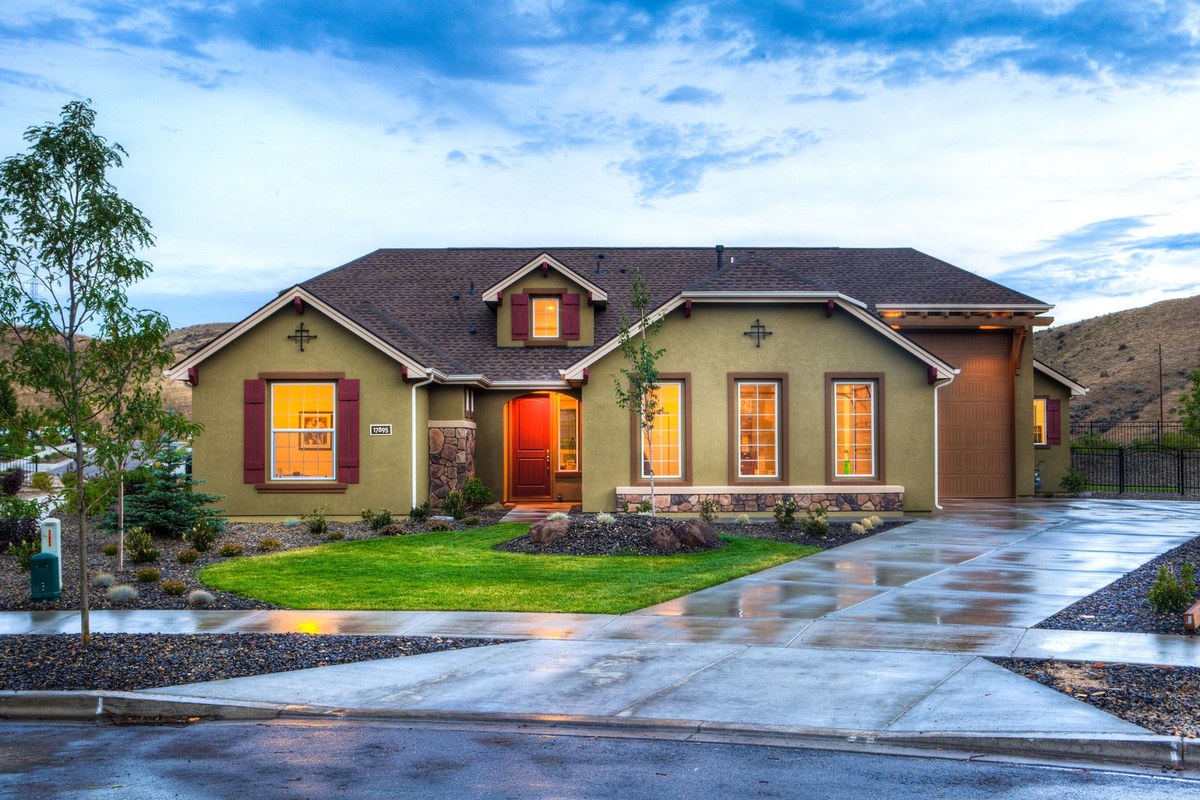 Single-story suburban home glowing at dusk with a green lawn, driveway, and rolling hills beyond.